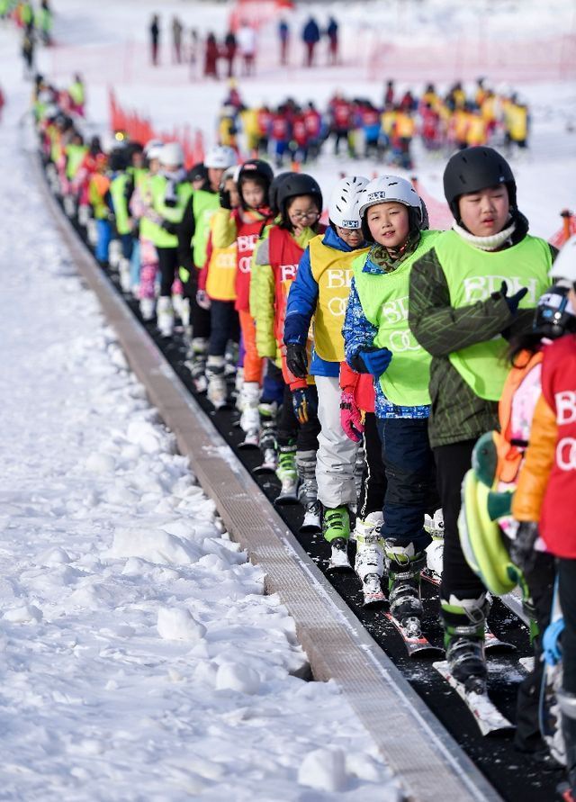 在吉林北大壶滑雪场，吉林市第二实验小学学生们在滑雪教练的带领下乘坐“魔毯”前往雪场学习区域。